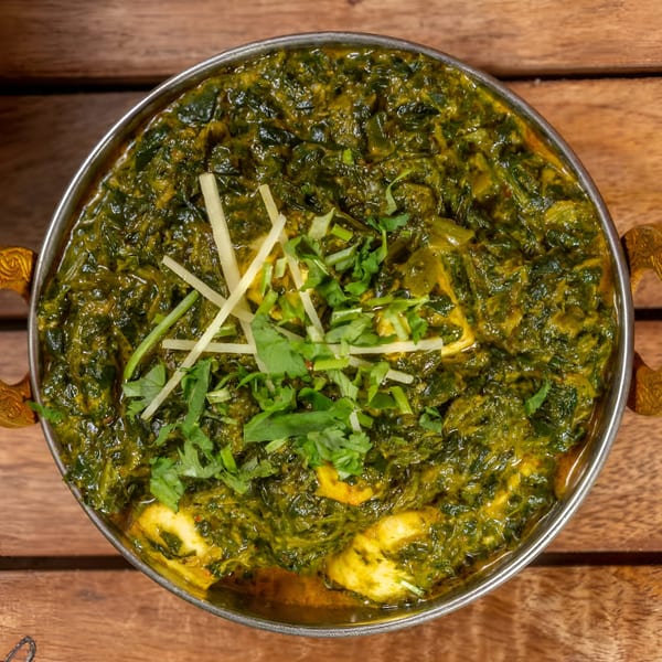 Palak Paneer, a vibrant green Indian spinach and cheese curry, garnished with ginger and cilantro.
