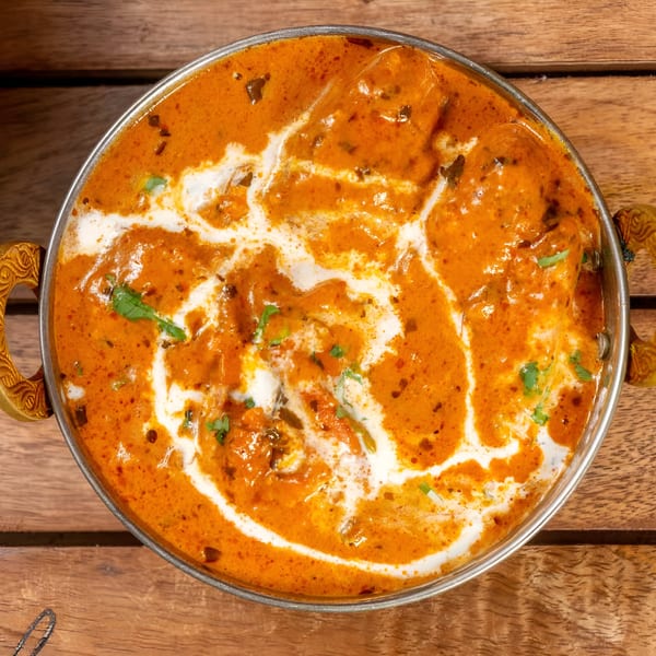 Overhead view of a copper bowl filled with vibrant orange Indian curry, drizzled with white cream.