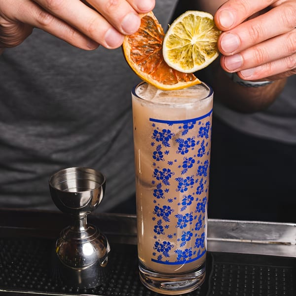 Hands garnishing a tall Indian cocktail with dried orange and lime slices at Bombay Street Foods.