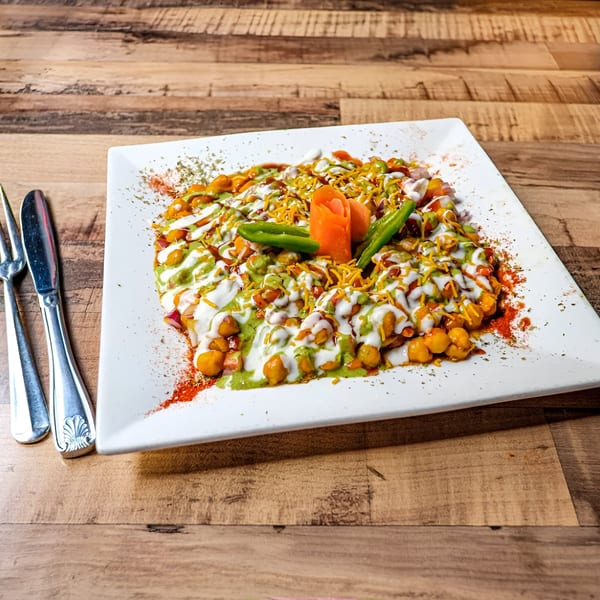 Bombay Street Foods' Chana Chaat, a chickpea dish with yogurt, chutneys, and spices on a white plate.