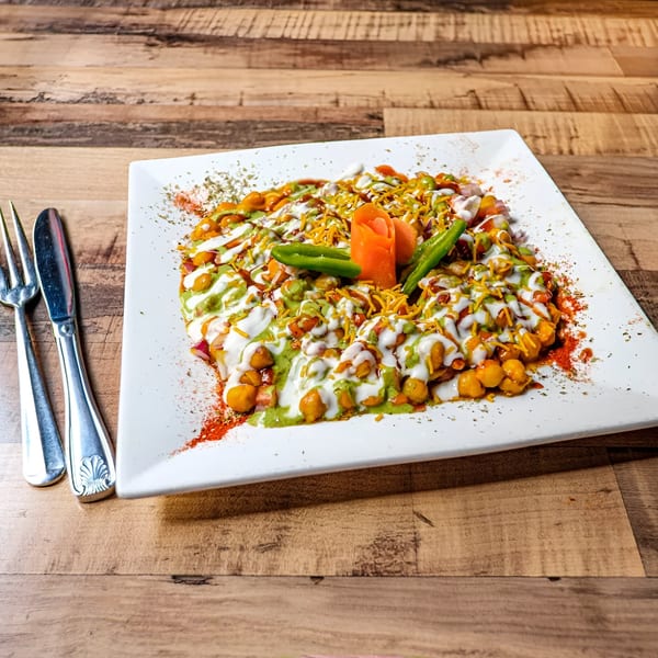 Bombay Street Foods' Indian chaat with chickpeas, sauces, and spices on a white plate.