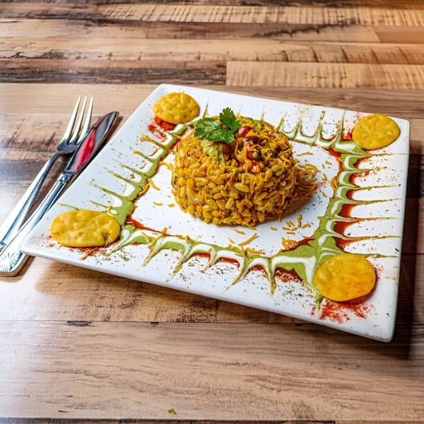 A Bombay Street Foods Bhel Puri dish, garnished with cilantro, on a white plate with cutlery.