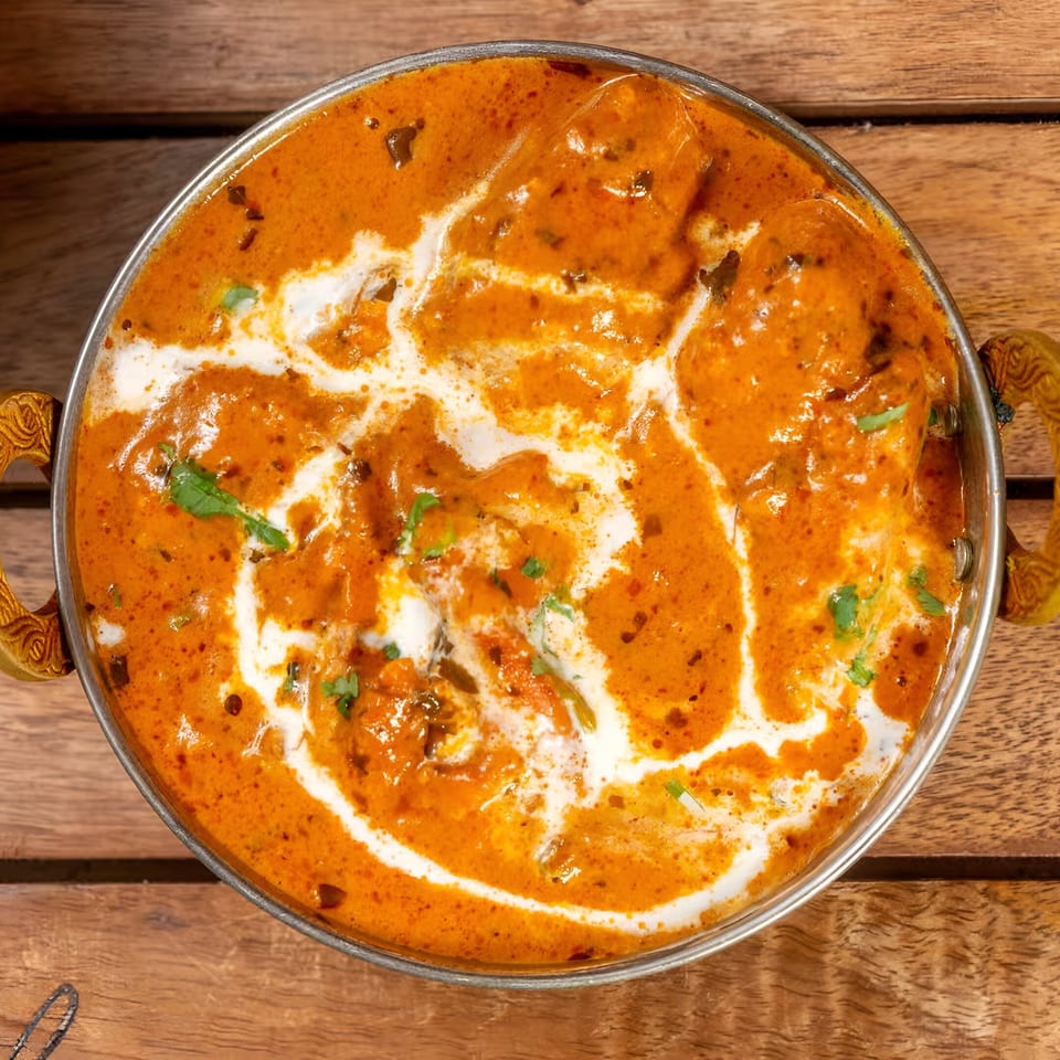 Overhead view of a metal bowl filled with vibrant orange Indian curry, swirled with white cream and garnished with cilantro.