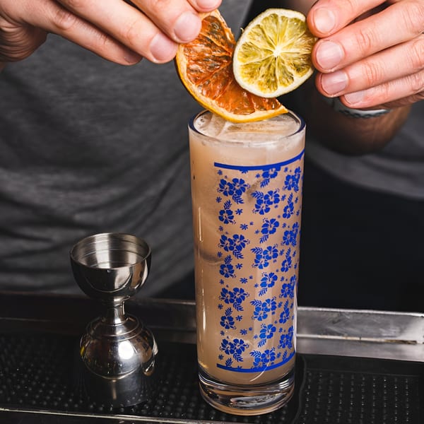 Hands garnishing a tall cocktail with dried orange and lime slices at Bombay Street Foods.