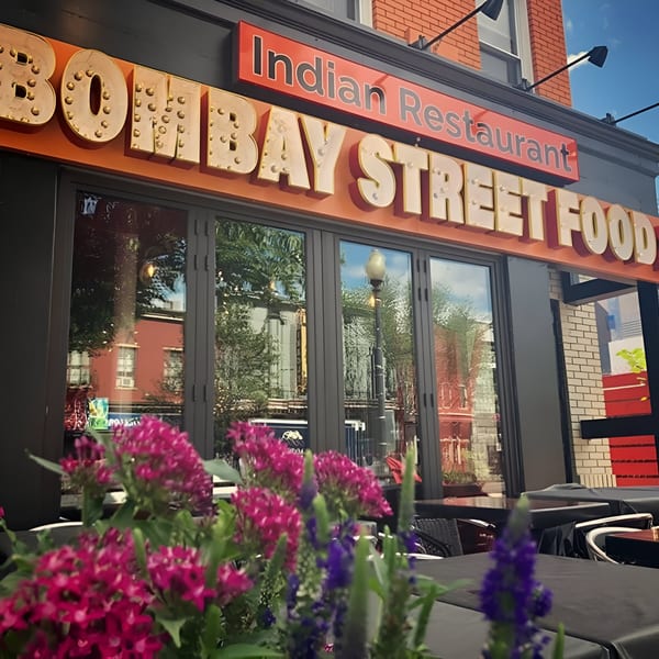 Exterior of Bombay Street Foods Indian restaurant with large windows and pink flowers in the foreground.
